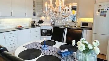 A modern kitchen with white cabinets, a chandelier, a dining table with black placemats, and a vase with white flowers.
