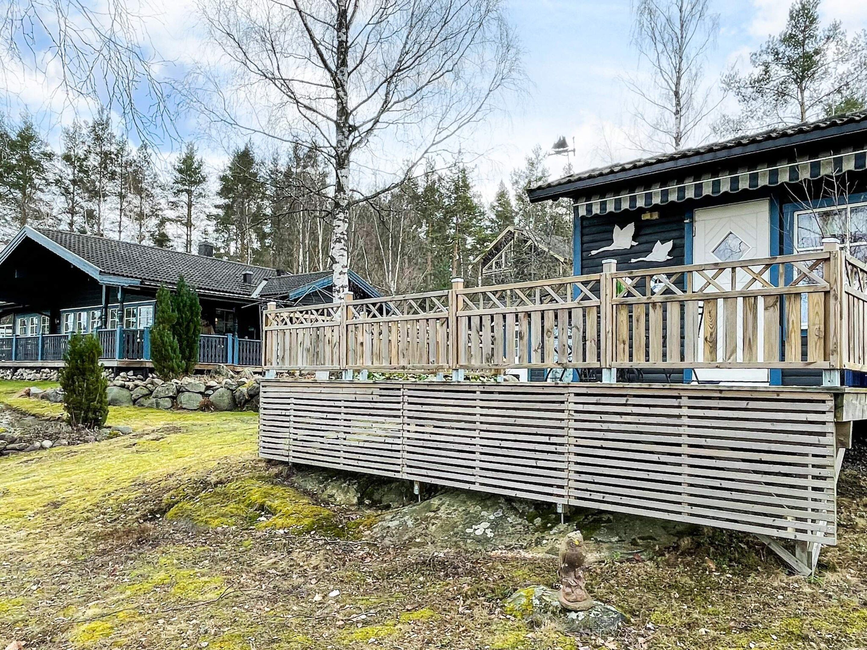 A cabin with a wooden deck, a small statue, and a building with a blue roof.
