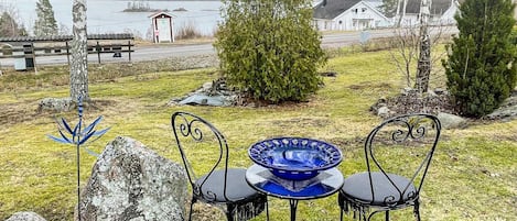 Una mesa con sillas y un tazón azul en un área verde con árboles y vista al lago.