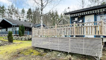 A wooden cabin with a fenced deck, surrounded by trees and a grassy area.