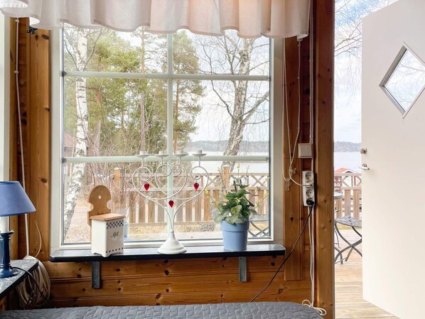 A room with a large window, a wooden bench, a potted plant, and a small table with a lamp.