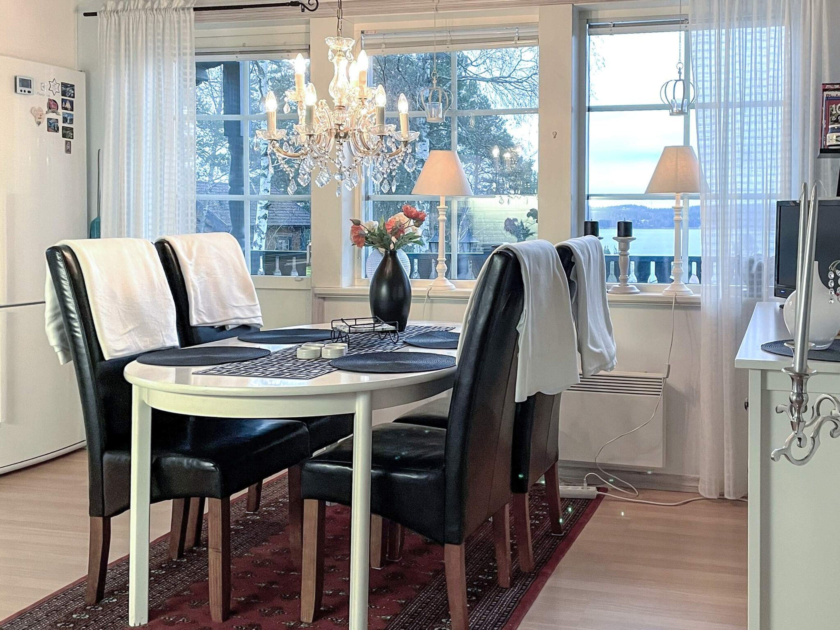 A dining area with a table, chairs, a chandelier, a vase with flowers, and a window with a view.