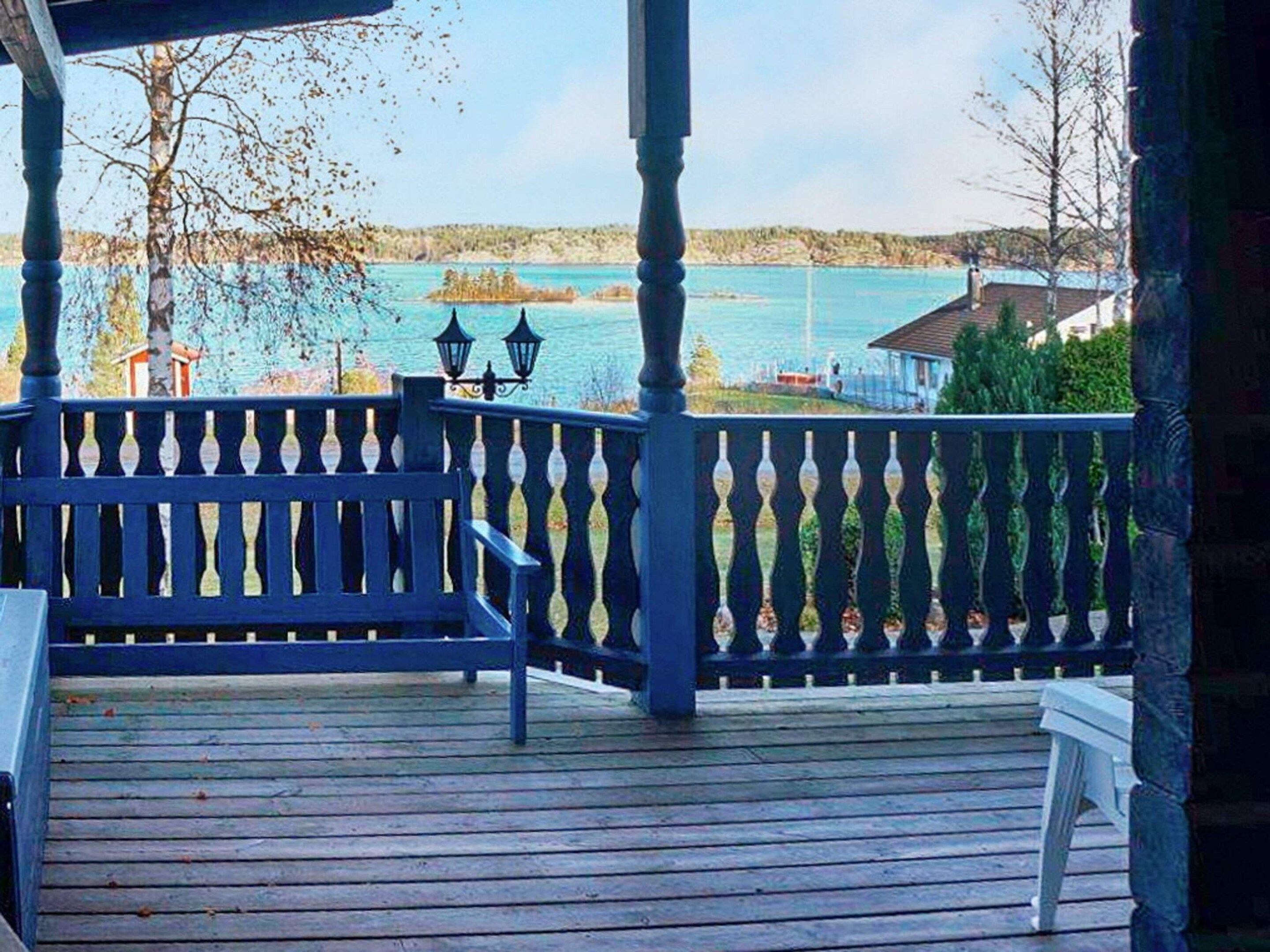 A wooden deck with a railing, overlooking a body of water and distant land.
