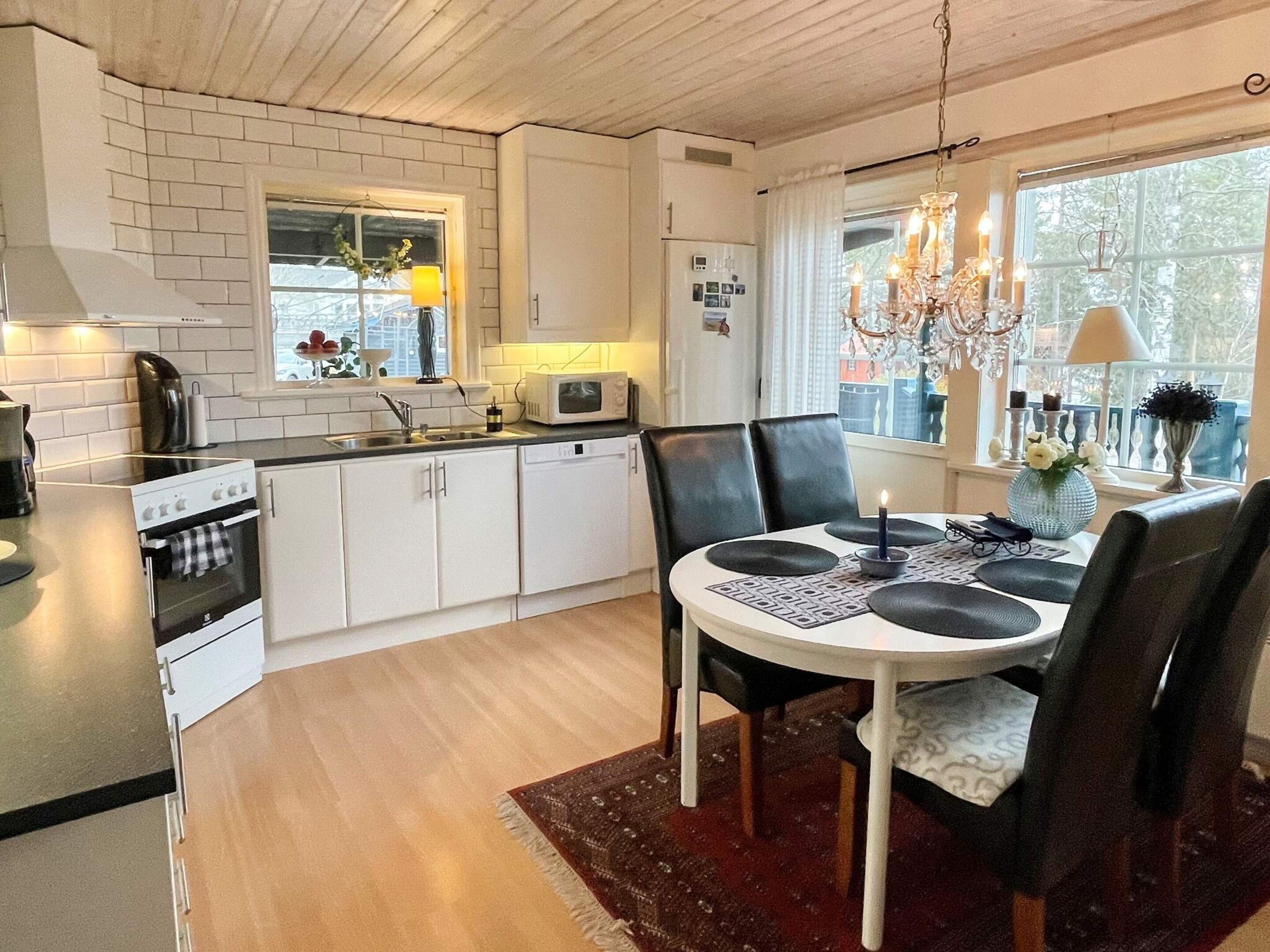 A modern kitchen with white cabinets, a microwave, and a stove. There is a dining area with a table and chairs, and a chandelier.