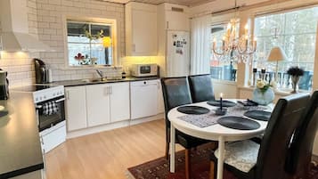 A modern kitchen with white cabinets, a microwave, and a stove. There is a dining area with a table and chairs, and a chandelier.