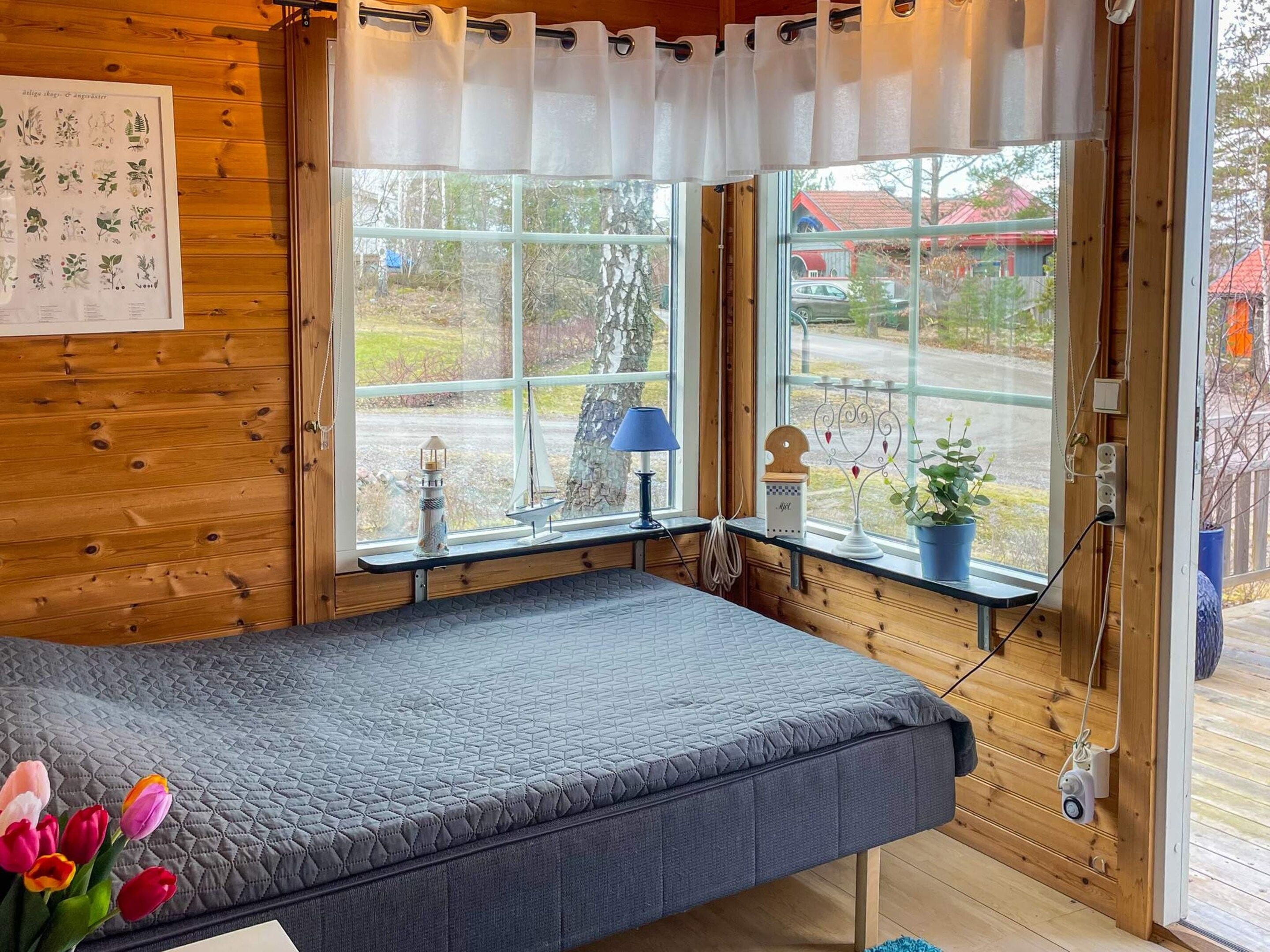 A room with a bed, a window with curtains, a wall-mounted shelf with decorative items, and a potted plant.