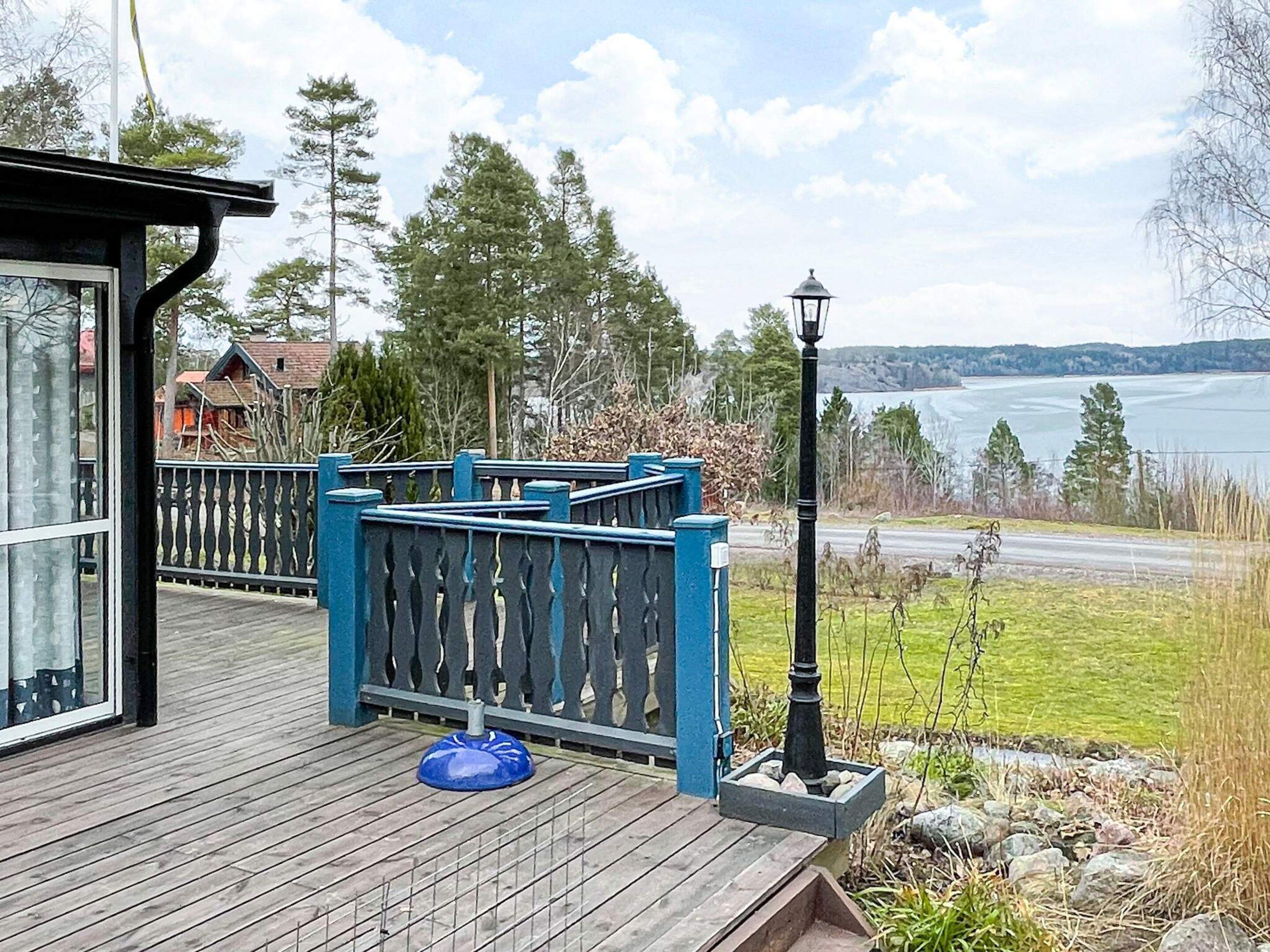 Um deck de madeira com guarda-corpo azul, um poste de luz e vista para um lago.