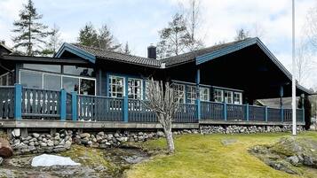 Une cabane avec des fondations en pierre, une terrasse en bois et un grand porche ouvert.