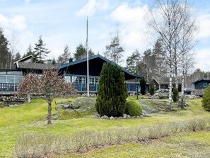 A cabin with a blue roof and a flagpole, surrounded by a grassy area with trees and rocks.