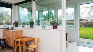 Une pièce lumineuse avec un bureau et des chaises en bois, de grandes fenêtres et des plantes en pot sur le rebord de la fenêtre.