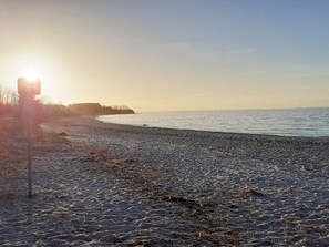 Ein Strand mit blauem Himmel und untergehender oder aufgehender Sonne.