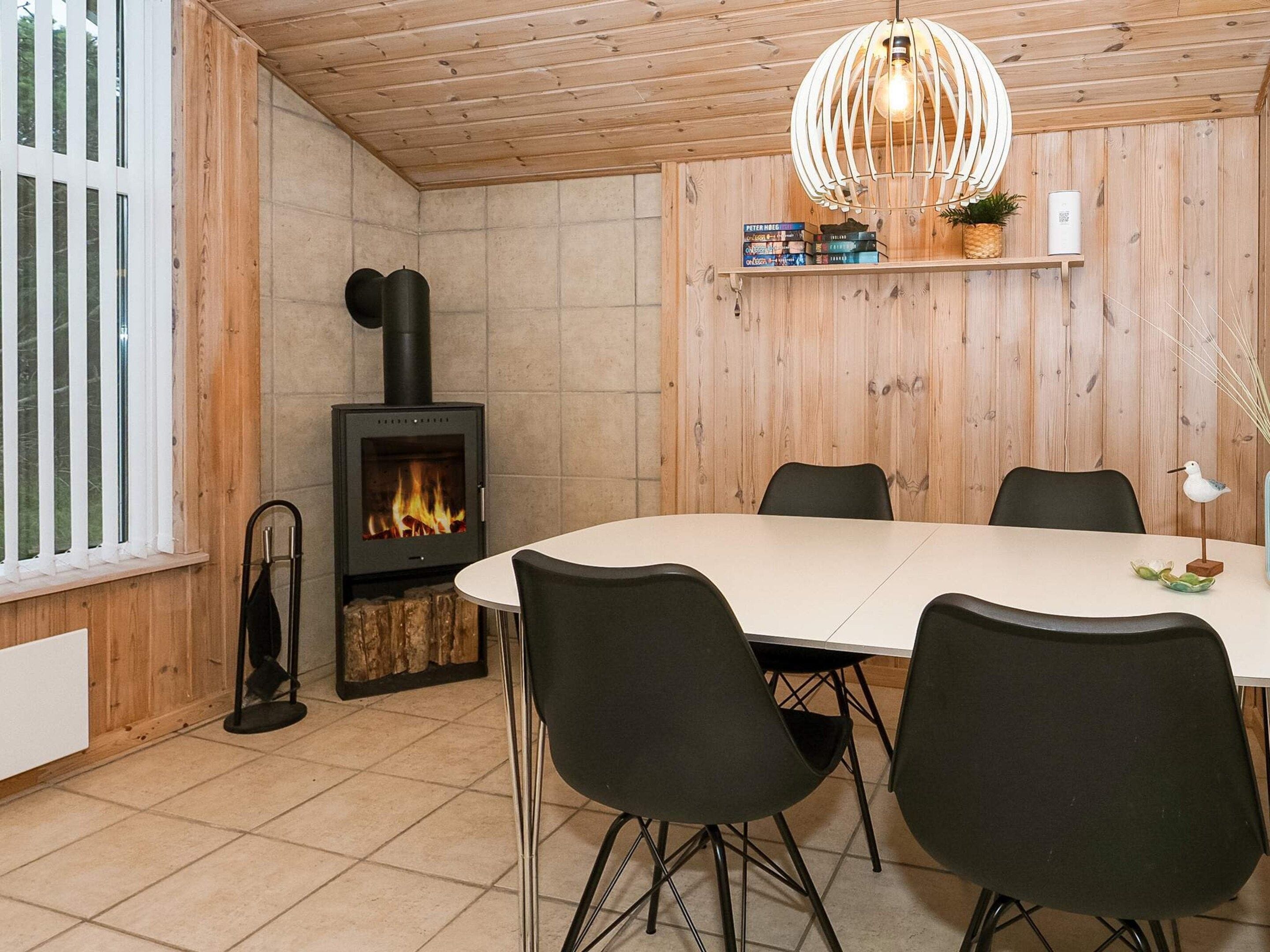 Et spiseområde med et rundt bord, fire stole, en brændeovn og en hængende lampe.