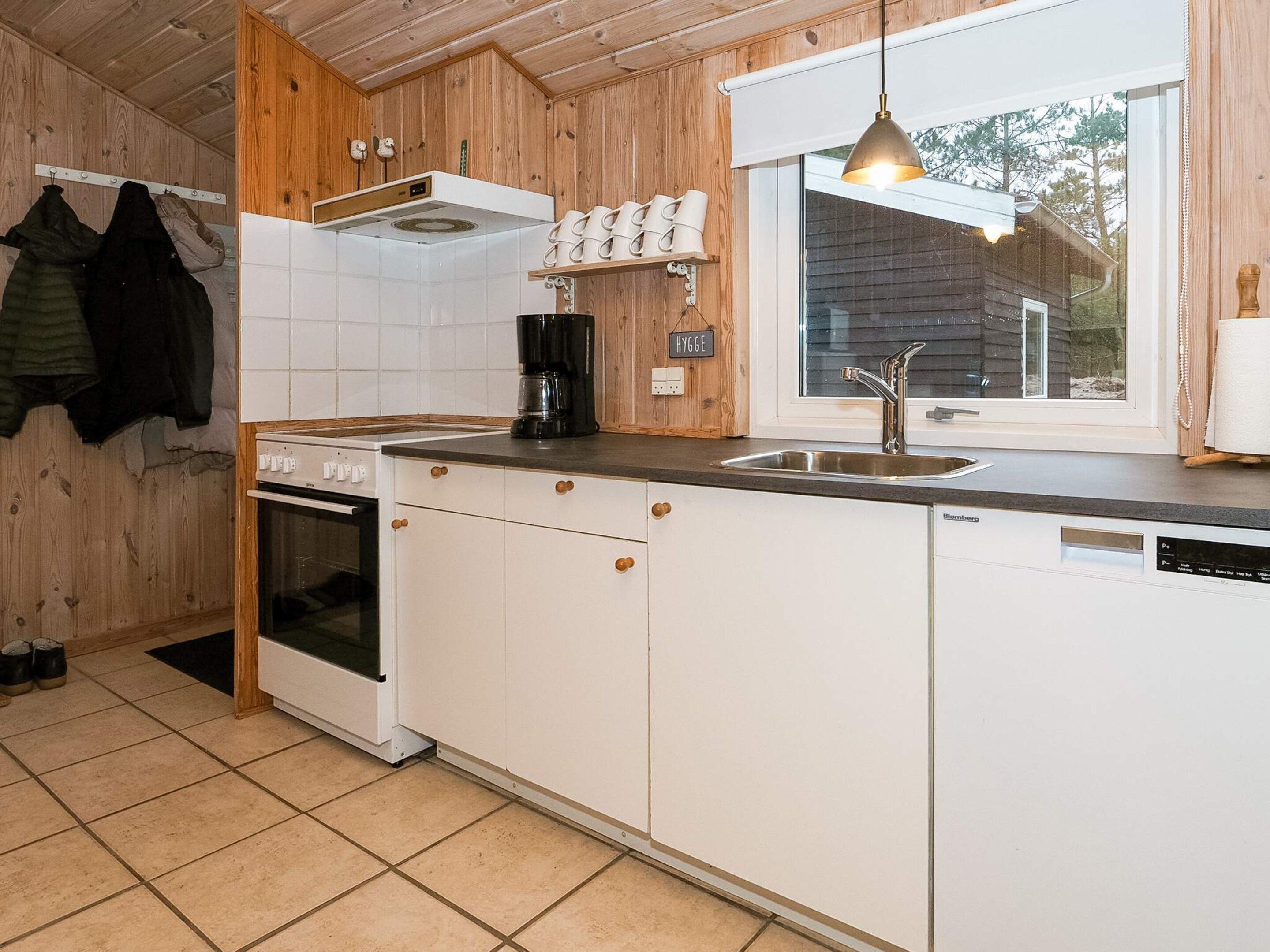 Eine Küche mit Holzschränken, einem Herd, einer Spüle und einem Fenster.