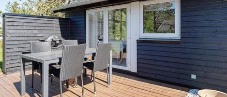 A deck with a table and chairs, a grill, and a sliding glass door leading to a covered area.