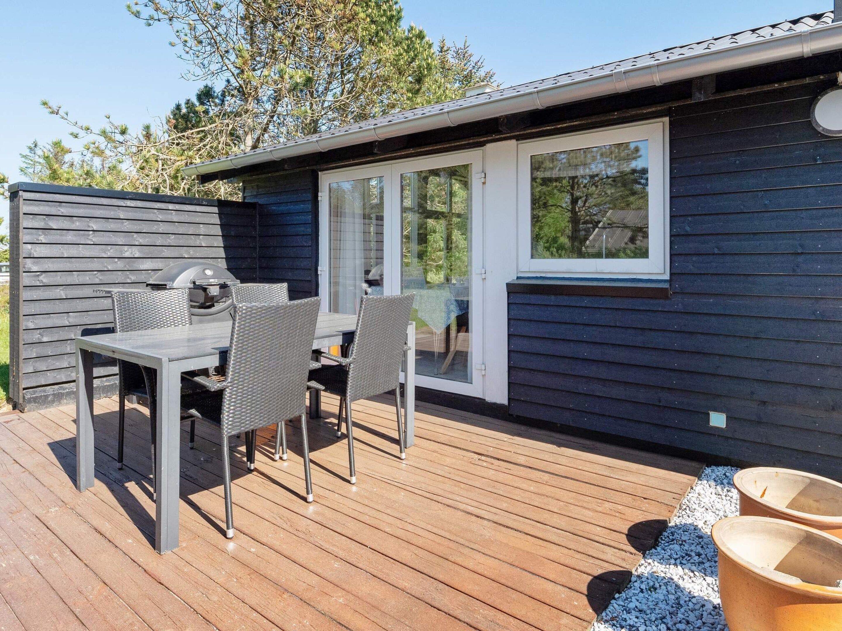 A deck with a table and chairs, a grill, and a sliding glass door leading to a covered area.