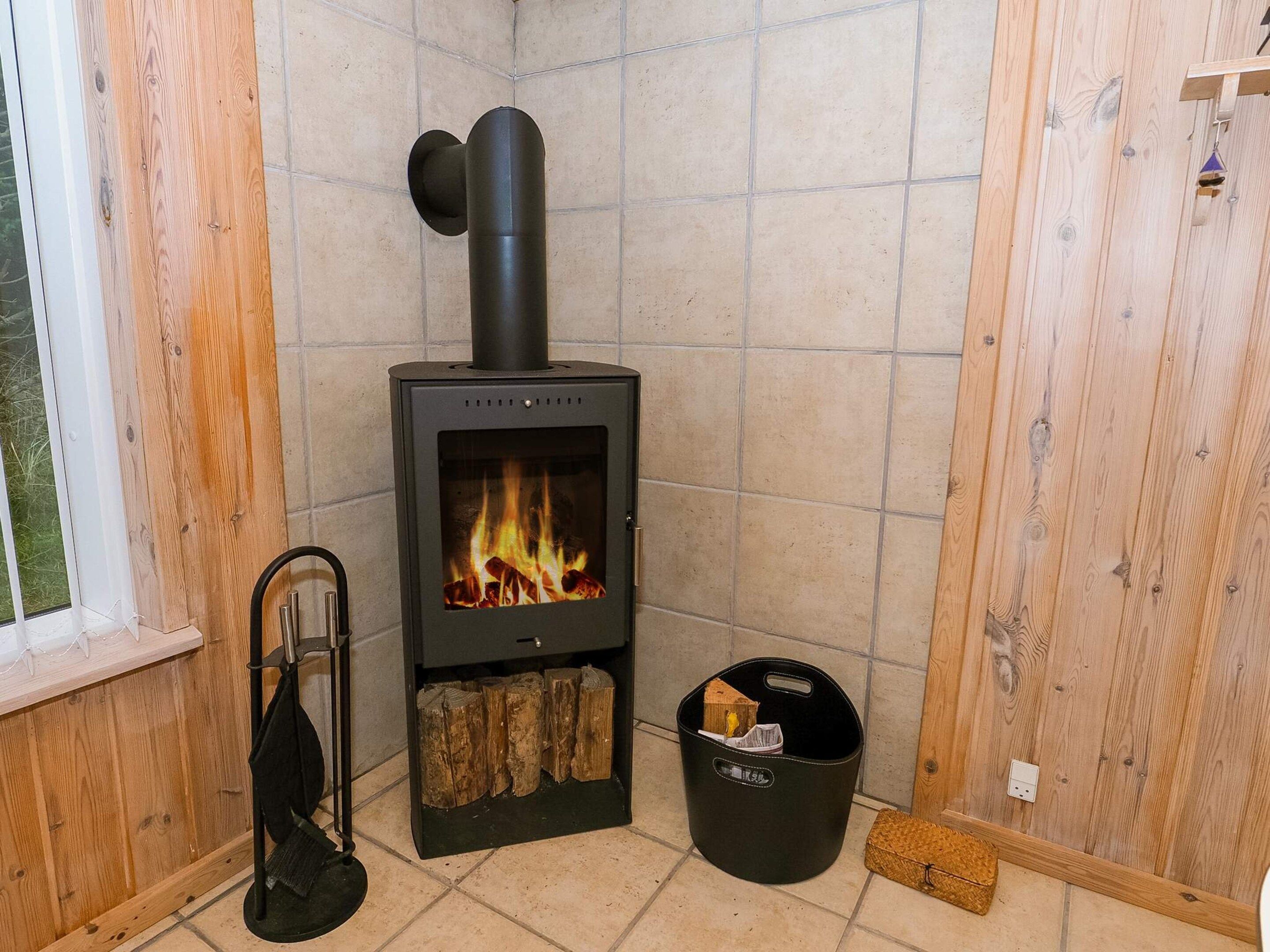Ett rum med en vedeldad kamin, ett fönster och en svart förvaringsbehållare.