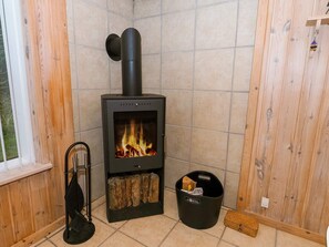 A room with a wood-burning stove, a window, and a black storage bin. - Serene Holiday Home in Jutland near Sea (Thisted)