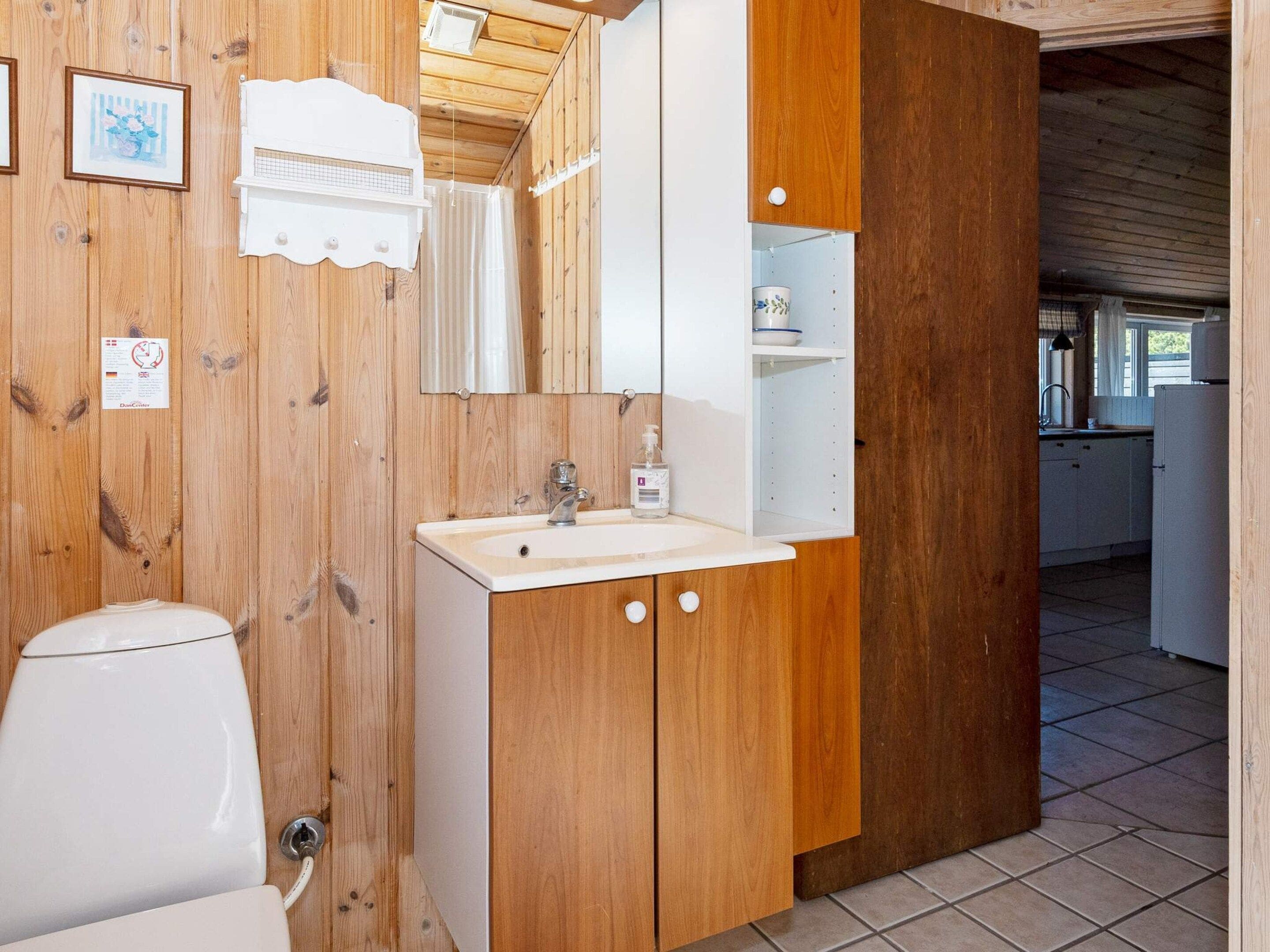 Ein Badezimmer aus Holz mit einem weißen Waschbecken, einem Spiegel und einer Duschkabine.