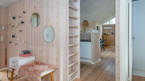 A modern interior with wooden panel walls, a white desk with a fluffy chair, and a kitchen area visible through an open door. - Spacious Holiday Home in Jutland With Whirlpool (Oksbol)