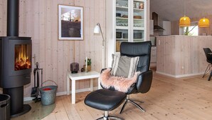 A cozy living room with a wood-burning stove, a black leather chair with a fluffy pillow, a white cabinet with glass doors, and a framed picture on the wall. - Spacious Holiday Home in Jutland With Whirlpool (Oksbol)