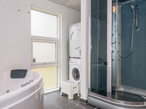 A compact bathroom with a bathtub, a washing machine, and a glass-enclosed shower area. - Spacious Holiday Home in Jutland With Whirlpool (Oksbol)