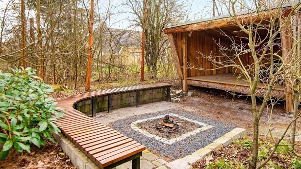 A wooden cabin with a fire pit in the center, surrounded by a gravel area and a wooden bench. - Spacious Holiday Home in Jutland With Whirlpool (Oksbol)