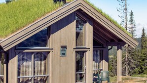 Une cabane en bois dotée de grandes fenêtres, d’une terrasse en bois et d’une enseigne indiquant « Varden Fjellandsby 210 ».