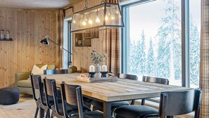 Un coin repas chaleureux avec une table en bois, des chaises noires et une grande fenêtre donnant sur des arbres couverts de neige.