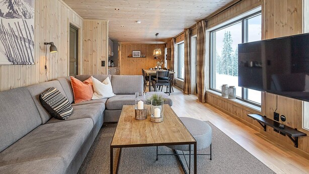 Un salon moderne avec un plafond en bois, une grande télévision, un canapé et un coin repas.