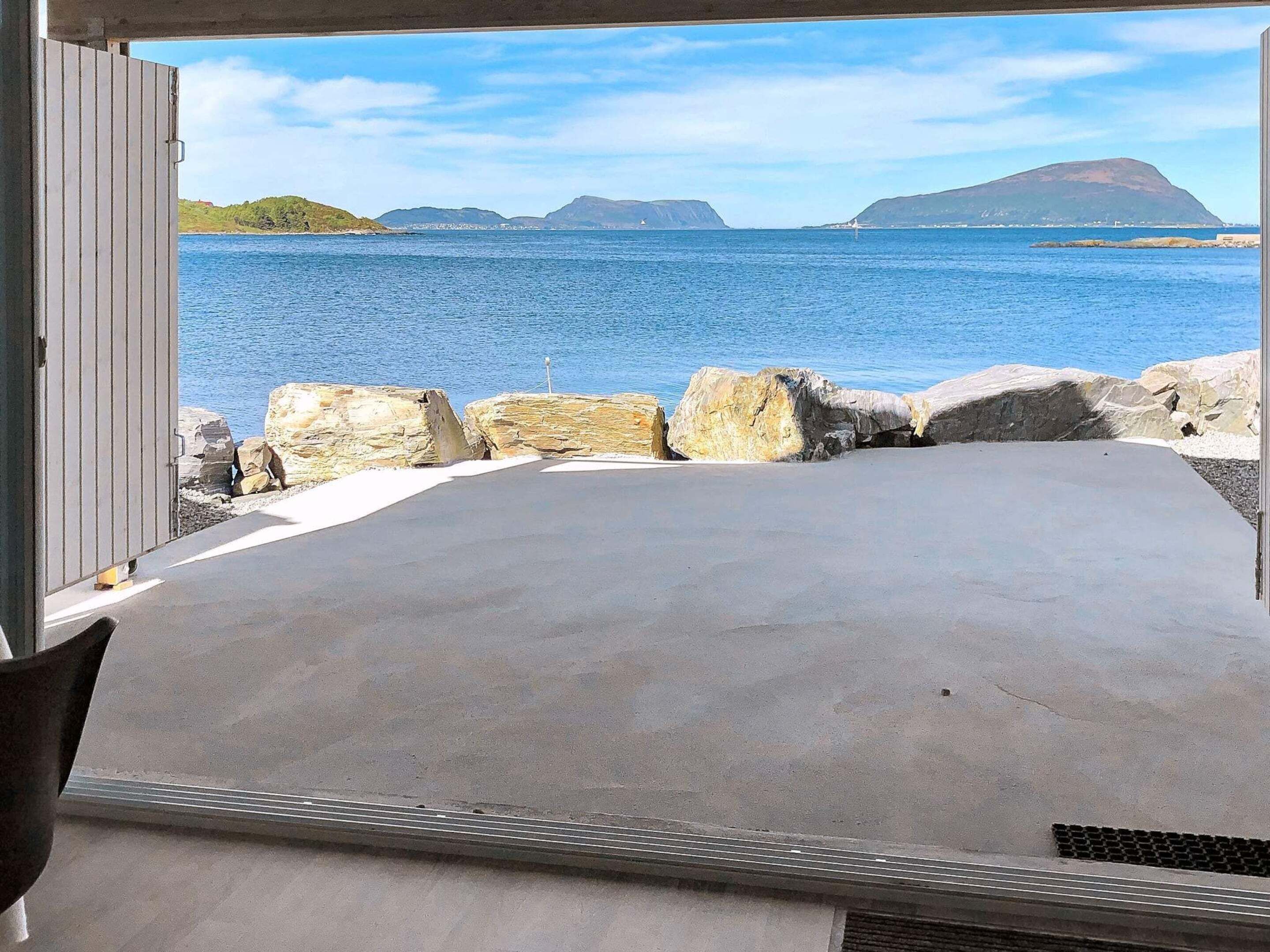 Une pièce avec un plancher en béton, une fenêtre donnant sur une étendue d’eau et une vue sur des collines lointaines.
