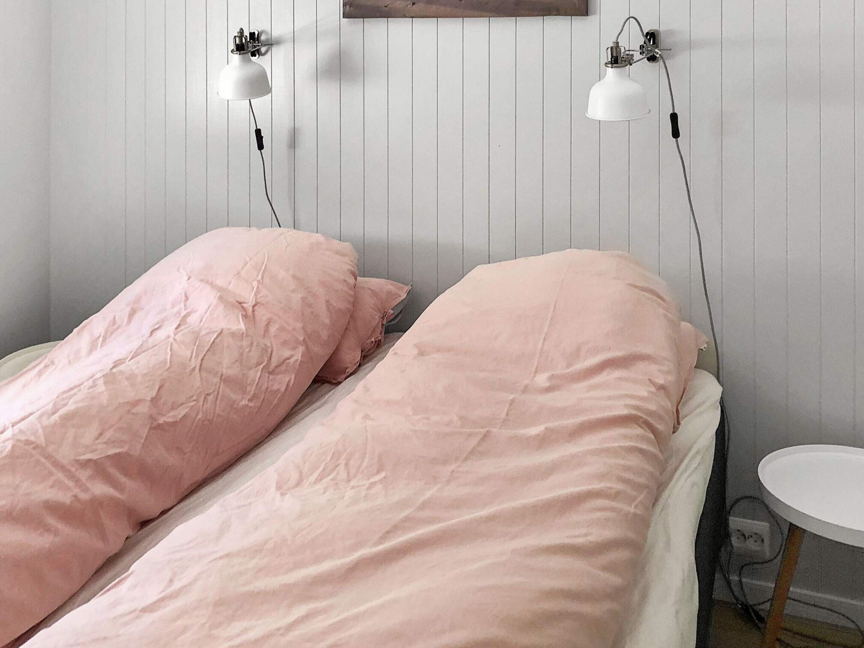 Een slaapkamer met twee eenpersoonsbedden, elk met roze beddengoed, een klein rond tafeltje en twee wandlampen.
