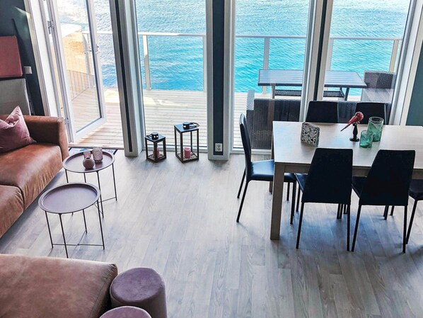 Ein modernes Interieur mit einem Balkon mit Meerblick, einem Essbereich mit Stühlen und Tisch sowie einer Sitzecke mit Sofa und Beistelltischen.