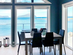 A dining area with a table and chairs facing a large window overlooking the sea. - 5 Star Holiday Home in Brattvag (Ålesund)