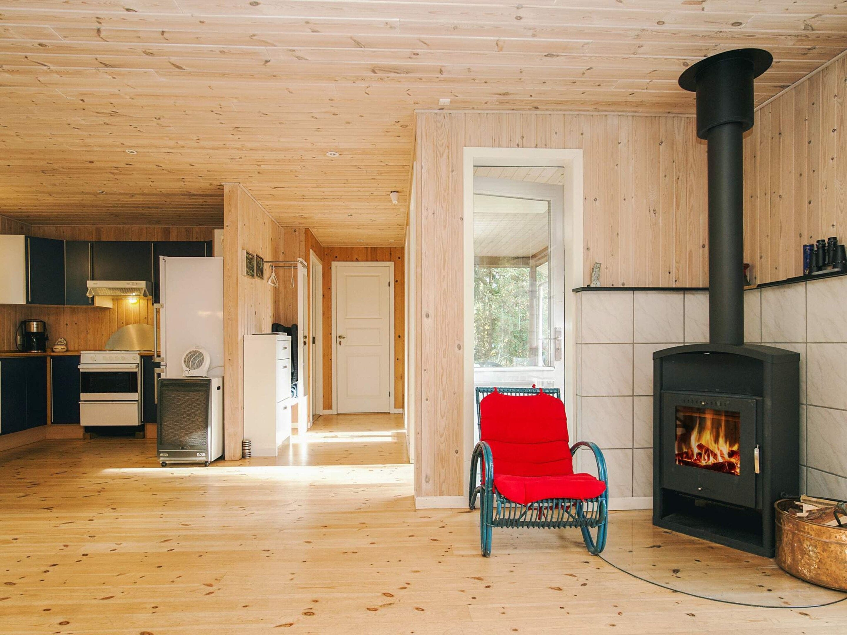 A wooden interior with a fireplace, a red chair, and a kitchen area.