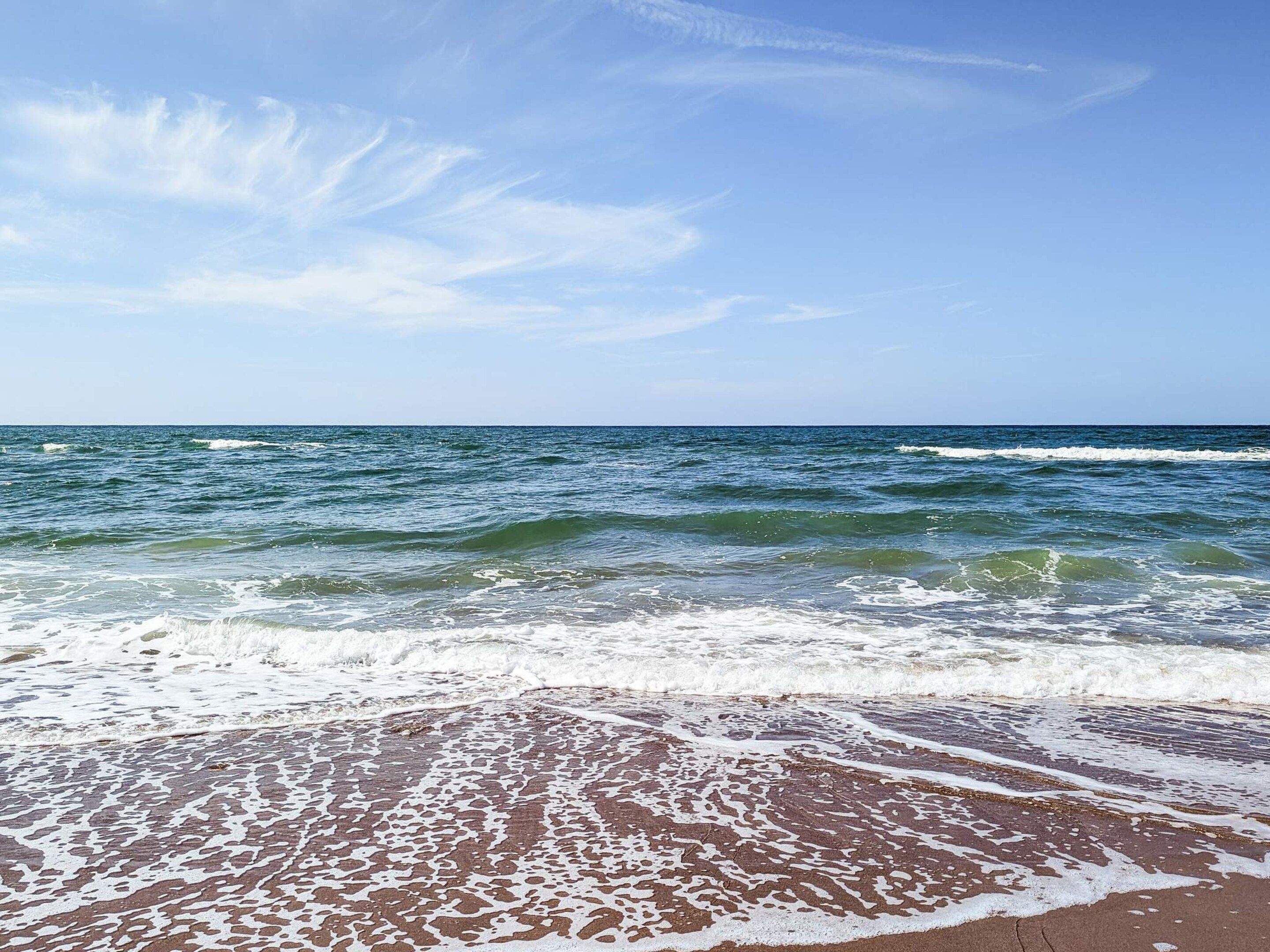 Ein Strand mit Wellen, blauem Himmel und weiter Fernsicht.