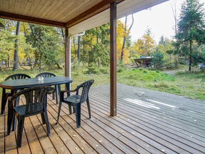 Une terrasse extérieure couverte, dotée d’une table et de chaises, et entourée d’une zone boisée.