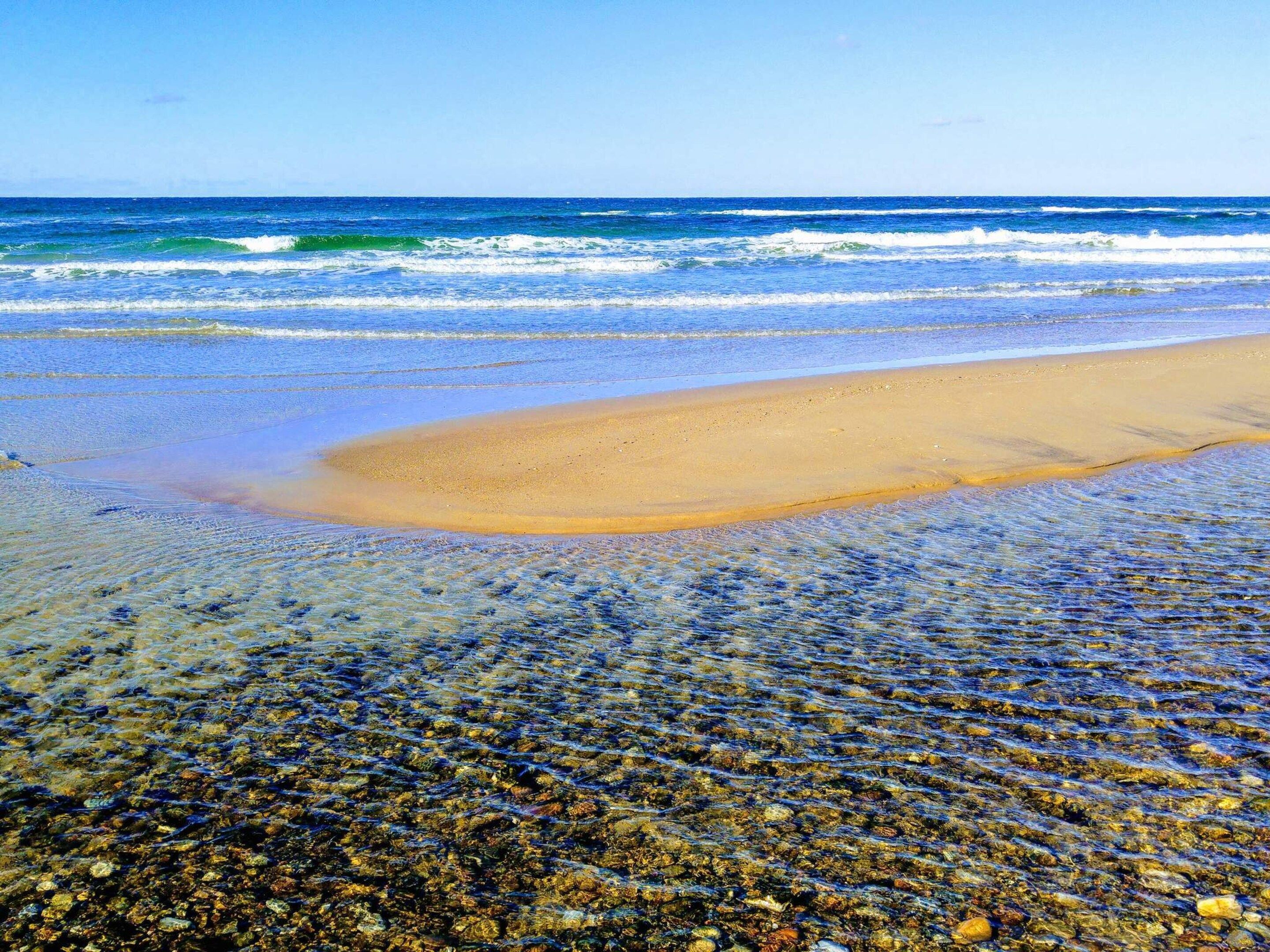 Een strand met helder water, kiezelstenen en een zandgedeelte.