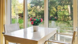 A table with a potted plant in a white pot, a chair, and a view of a garden through large windows. - 8 Person Holiday Home in Frederiksvaerk (Frederiksvaerk)