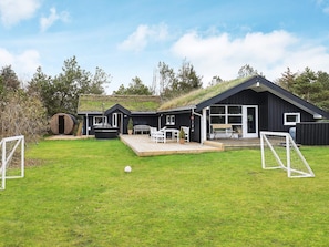 A modern black building with a large deck, a hot tub, and a soccer goal in the yard.