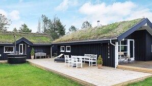 A row of black cabins with a wooden deck, white furniture, and a grassy area. - Spacious Holiday Home in Jutland With Outdoor Whirlpool (Pandrup)