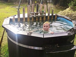 Een kind in een houten hot tub met een houten terras en een tafel.
