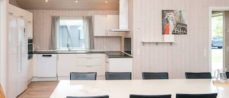 A modern kitchen with white cabinets, a large island, and black chairs around a white table.