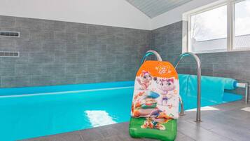 Una piscina con tobogán, paredes de azulejos grises y un ventanal.