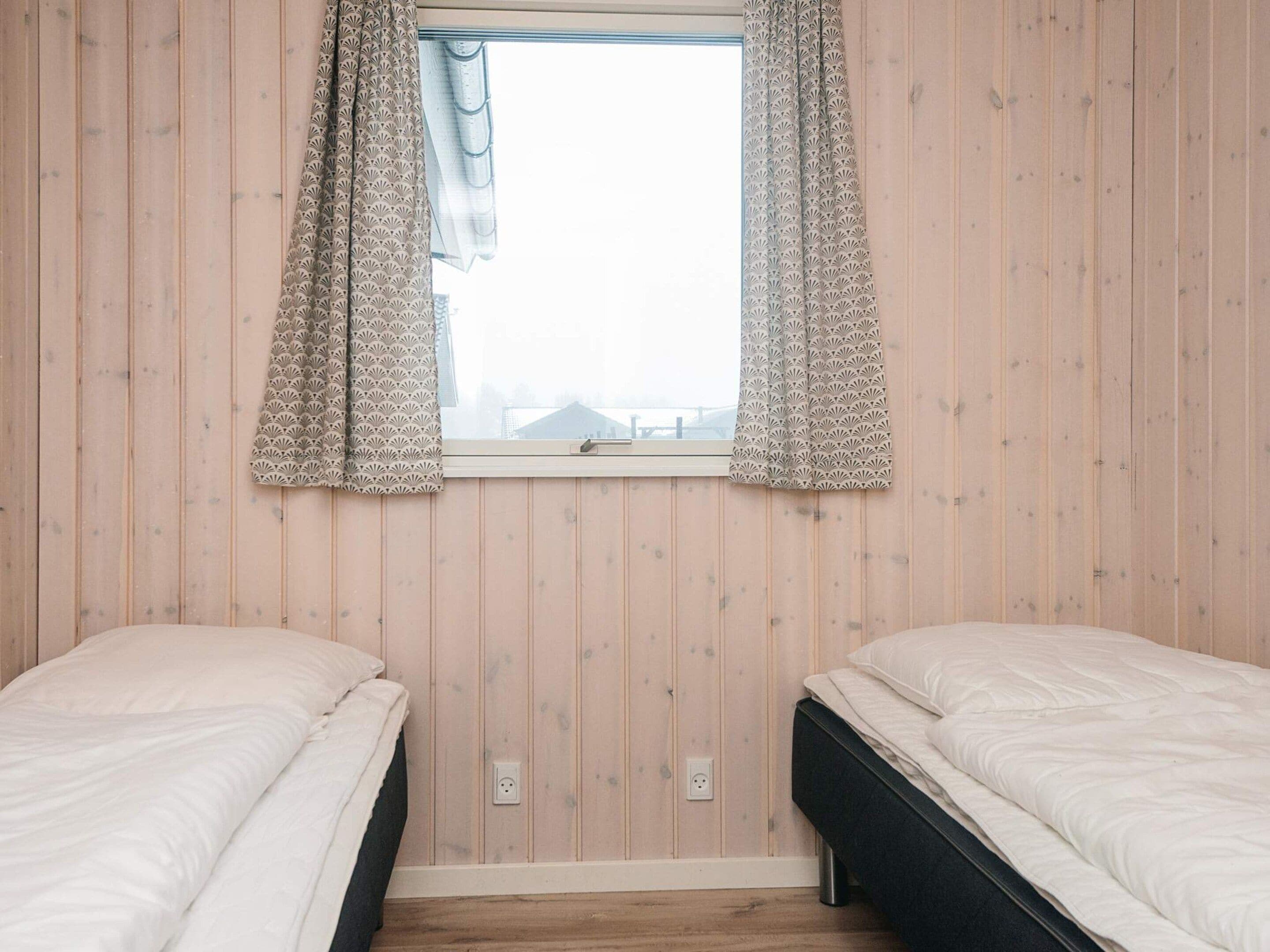 Habitación con dos camas, una ventana con cortinas estampadas y paredes de madera.