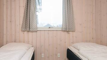 Habitación con dos camas, una ventana con cortinas estampadas y paredes de madera.