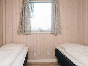 A room with two beds, a window with patterned curtains, and wooden walls. - 4 Star Holiday Home in Romo (Rømø)