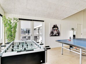 A room with a foosball table, a ping pong table, and a wall-mounted artwork.
