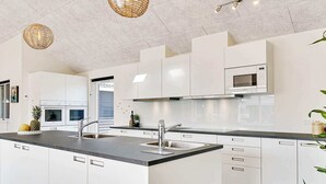 A modern kitchen with white cabinetry, a central island with a sink, and overhead lighting. - 5 Star Holiday Home in Grenaa (Grenaa)