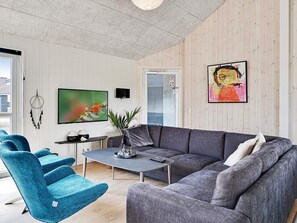 A modern living room with a grey sofa, blue armchairs, a coffee table, a flat-screen TV, and a painting on the wall.
