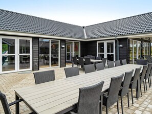 An outdoor patio with a long table and chairs, surrounded by glass doors and windows. - 5 Star Holiday Home in Grenaa (Grenaa)